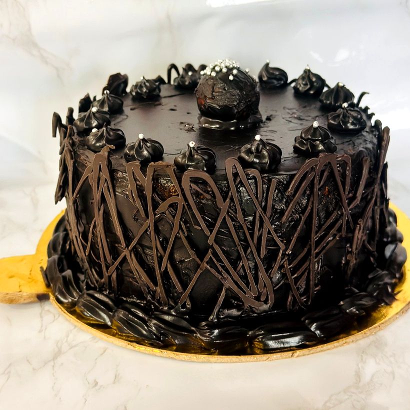 A tall chocolate truffle cake with a chocolate lattice around the sides, rosettes and a truffle ball on top