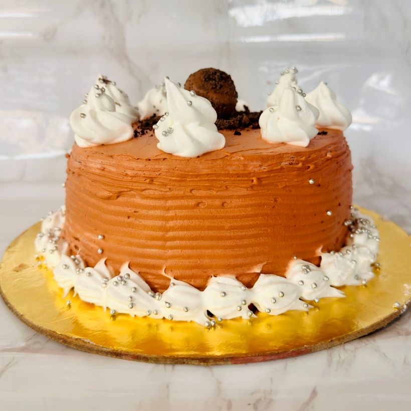 A vanilla cake finished with chocolate cream, white whipped-cream rosettes, silver pearls and a truffle ball
